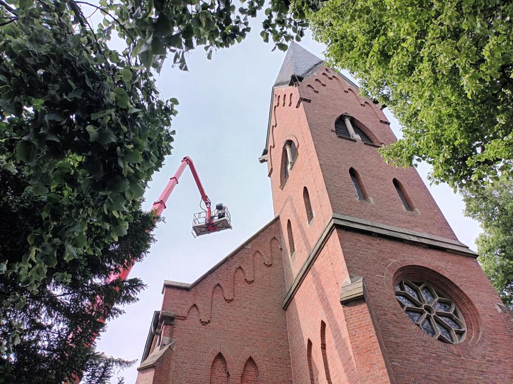 Dachdecker versuchen am Ende erfolgreich das 1,5 m x 1,5 m große Loch im Dach der Kirche zu flicken.